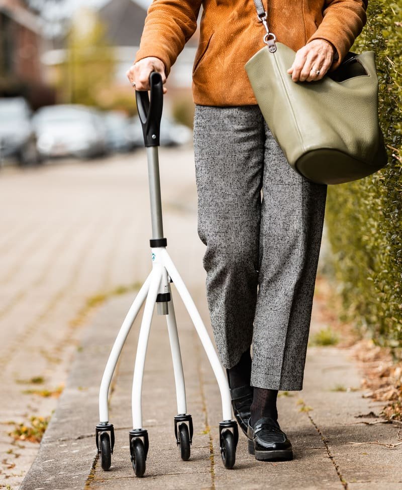 Persona adulta mayor caminando de forma autónoma por la calle, apoyada en un rollator.
